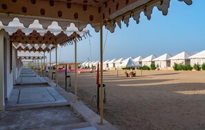 A covered walkway leading to a row of white tents. - Shama Desert Camp (Jaisalmer)