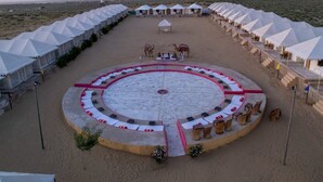 Un espacio de descanso al aire libre con asientos circulares, con cojines blancos y rojos, rodeado de tiendas de campaña y una estructura central.