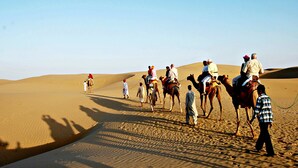 Un grupo de personas cabalgando camellos a través de un paisaje desértico con dunas de arena.