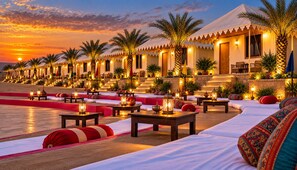 A hotel with outdoor seating areas, palm trees, and a sunset view. - Shama Desert Camp (Jaisalmer)