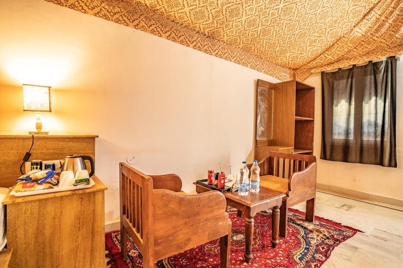 Una habitación acogedora con un escritorio de madera, sillas, una mesita pequeña y una alfombra estampada.