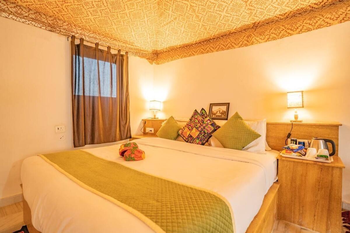 Habitación de hotel con una cama grande, dos mesitas de noche, techo estampado y una ventana con cortinas.