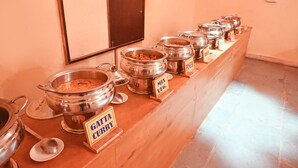 Un mostrador de buffet con recipientes etiquetados de comida, incluyendo 'GATTA CURRY' y 'MIX VEG'.