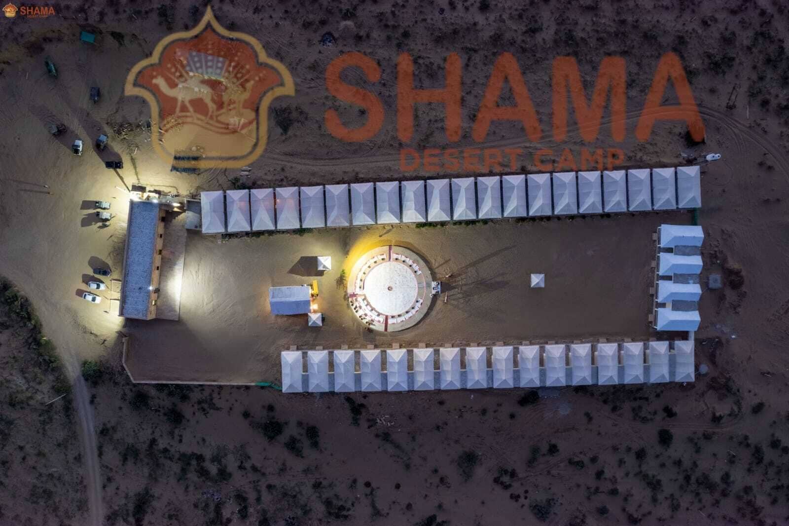 An aerial view of Shama Desert Camp with tents arranged in rows, a central circular structure, and a logo at the top.