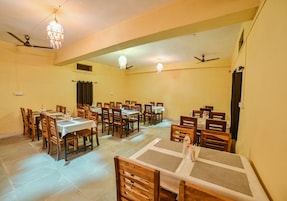 Uma sala de jantar com várias mesas e cadeiras, ventiladores de teto e luminárias pendentes.