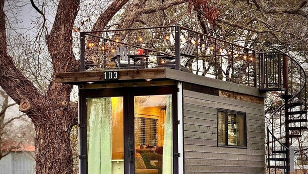 Eine kleine Hütte mit Glastür, Balkon und Treppe.