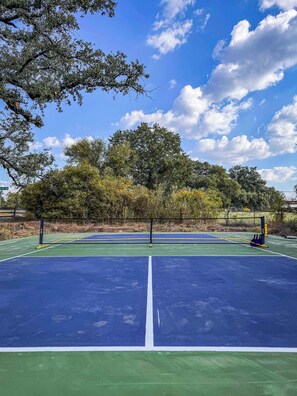 An outdoor tennis court with a net, surrounded by trees and a clear sky.