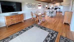 A spacious living area with a wooden ceiling, a dining table with chairs, a TV, and a kitchen in the background. - Sassy Seagull Beachfront and Sunrise (Grand Isle)