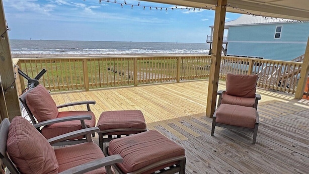 A wooden deck with four cushioned chairs and a small table, overlooking a beach. - Sassy Seagull Beachfront and Sunrise (Grand Isle)