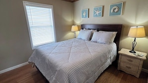 A bedroom with a bed, two bedside lamps, a nightstand, and three wall art pieces. - Sassy Seagull Beachfront and Sunrise (Grand Isle)