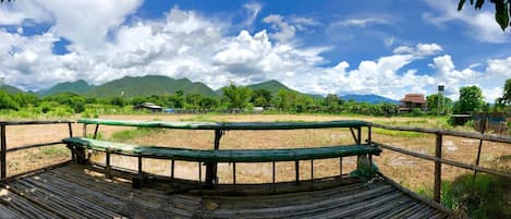 A bamboo deck with a view of a rural landscape, including mountains and scattered buildings.