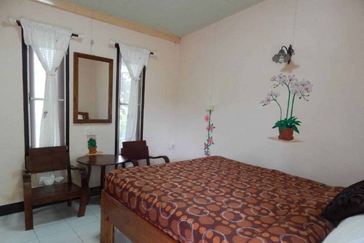 Un dormitorio con una cama, una silla, una mesita, un espejo y una planta en maceta.