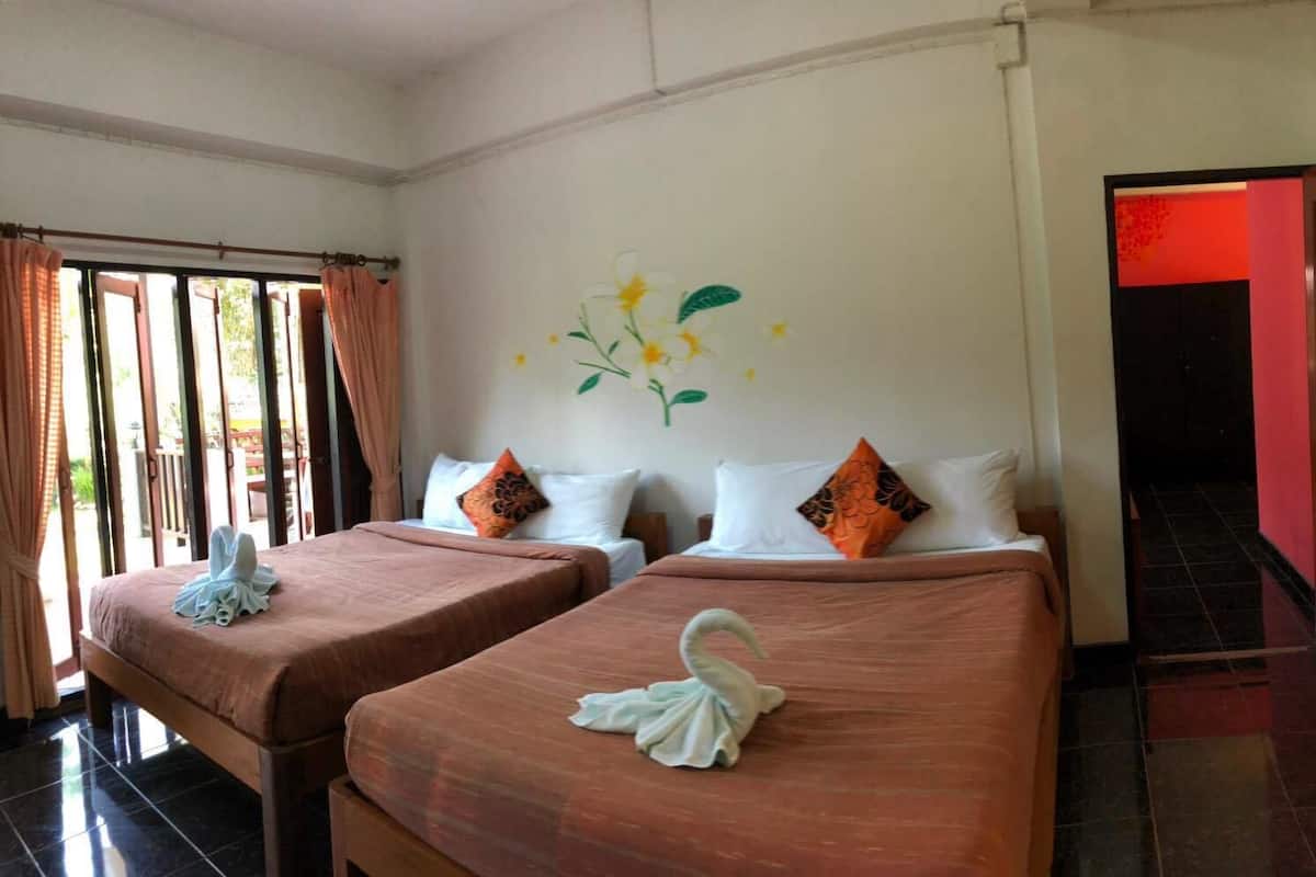 Habitación de hotel con dos camas, cada una con cubrecama marrón y almohadones decorativos. Hay un cuadro de flores en la pared y una puerta que da a otra habitación.