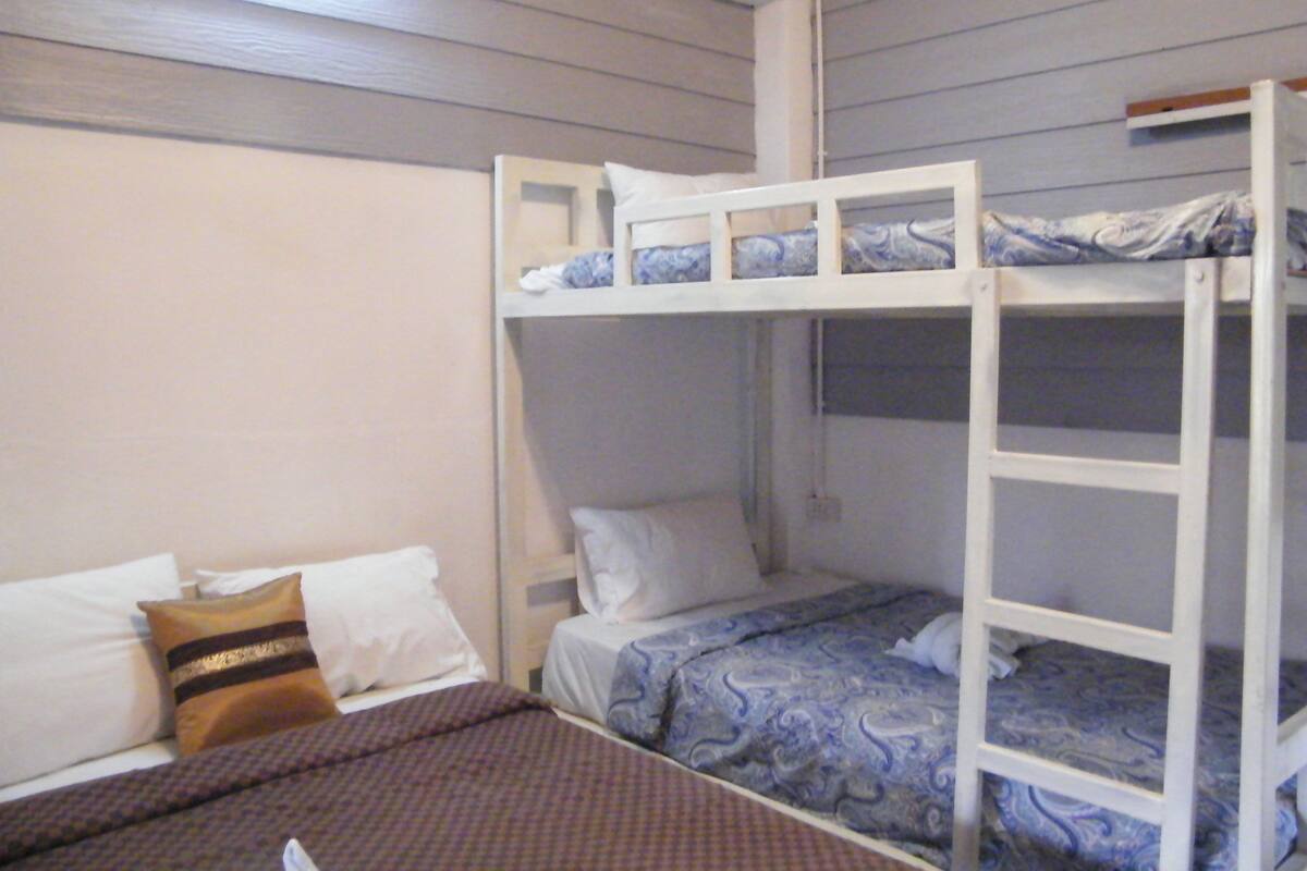 Dormitorio con literas, dos camas, una colcha marrón estampada y almohadas blancas.