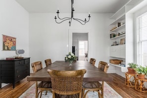 A dining room with a wooden table, wicker chairs, a chandelier, and white walls. - Restored 1930s Uptown Bungalow 2 min. to Magnolia (Waco)