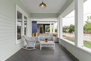 Eine Veranda mit einem Schaukelstuhl, einem kleinen Tisch mit einem Blumentopf und Blick auf die Straße.
