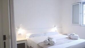 Et hotelværelse med en stor seng, hvide sengetøj, to sengeborde med lamper og et vindue med udsigt.