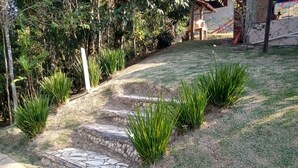 A garden with stone steps leading up to a house, surrounded by greenery and a paved path. - Sitio Oliveira Ibiúna (Ibiuna)