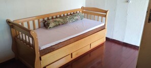 A wooden bed with a mattress and a pillow, a wooden drawer, and a white wall.