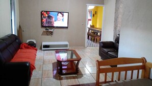 A living room with a TV, sofa, coffee table, and a dining area with a bench. - Sitio Oliveira Ibiúna (Ibiuna)
