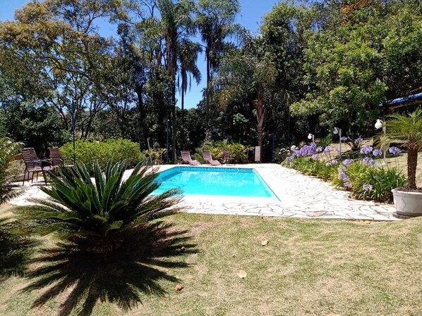 A rectangular swimming pool surrounded by a stone deck, with lounge chairs and a small table nearby.