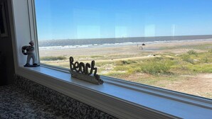 Uitzicht vanuit een raam op een strand, met een klein beeldje op de vensterbank.