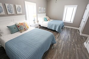 A bedroom with two beds, a nightstand, and a window. - Family Tides - Beachfront - Island Realty (Grand Isle)