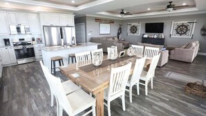 Een ruime keuken met witte kastjes, een groot eiland en een eethoek met witte stoelen.