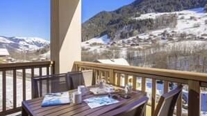Una terraza de madera con una mesa para dos, con vistas a un paisaje montañoso nevado.