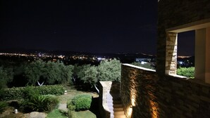 Nachtsicht von einem Steinhaus mit Fensterblick auf einen Garten und eine Stadtansicht.