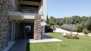 Ein modernes, zweistöckiges Haus mit Steinverkleidung, einer Veranda und einem Rasen mit zwei Liegestühlen.