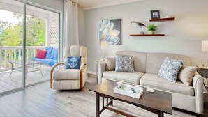Ein Wohnzimmer mit Sofa, Sessel, Couchtisch und einem Balkon mit Glastür.