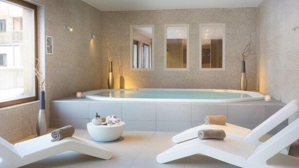 A modern spa room with a large bathtub, two lounge chairs, a bowl of toiletries, and a window providing natural light. - Vos Prochaines Vacances de Ski | Appart Confortable avec Cuisine (Arêches Beaufort)