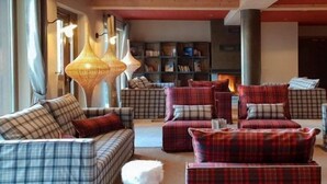 A cozy living room with plaid sofas and armchairs, a small stool, and a bookshelf in the background. - Vos Prochaines Vacances de Ski | Appart Confortable avec Cuisine (Arêches Beaufort)