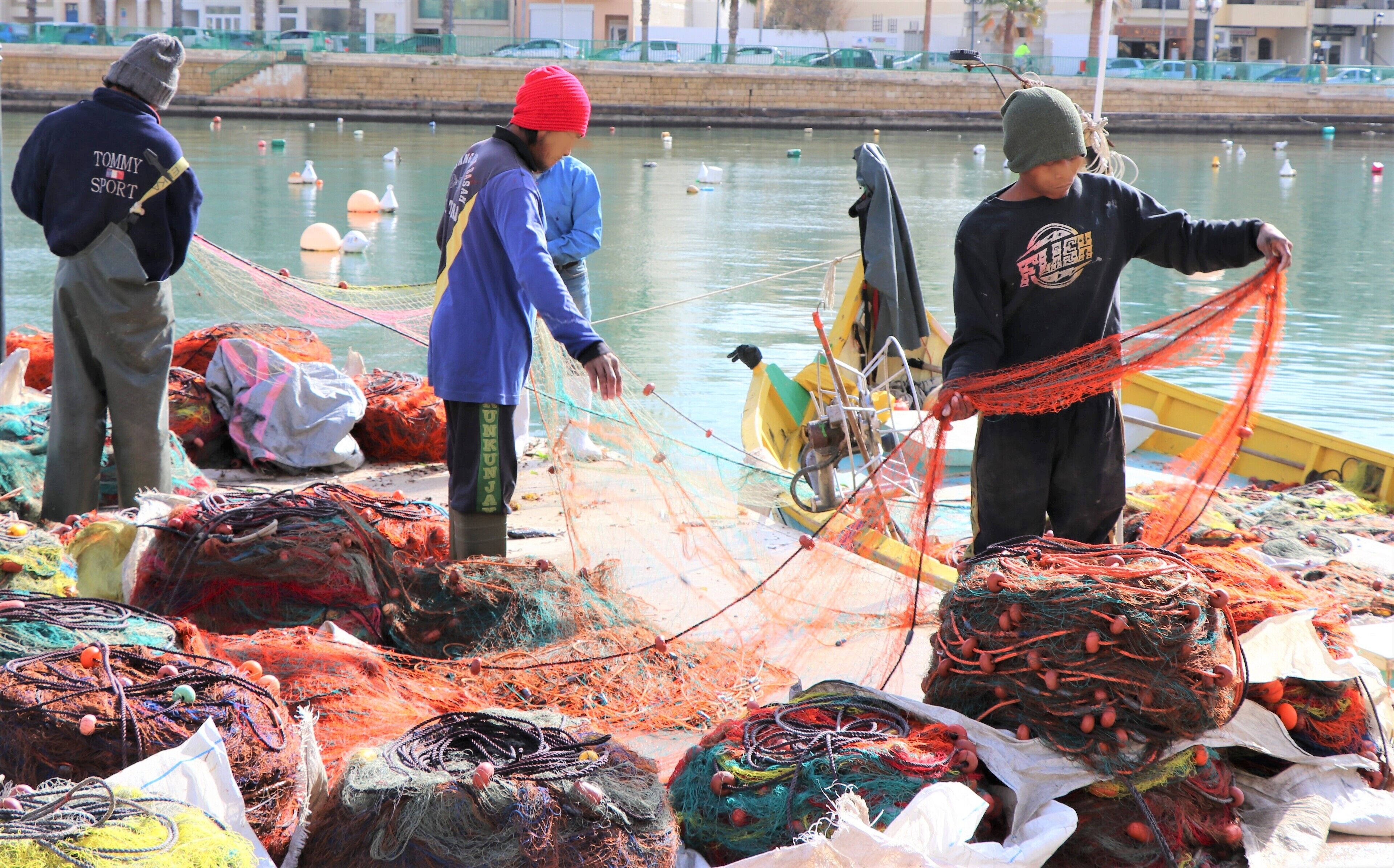 Un muelle con redes y equipos de pesca, una masa de agua y un puente al fondo.