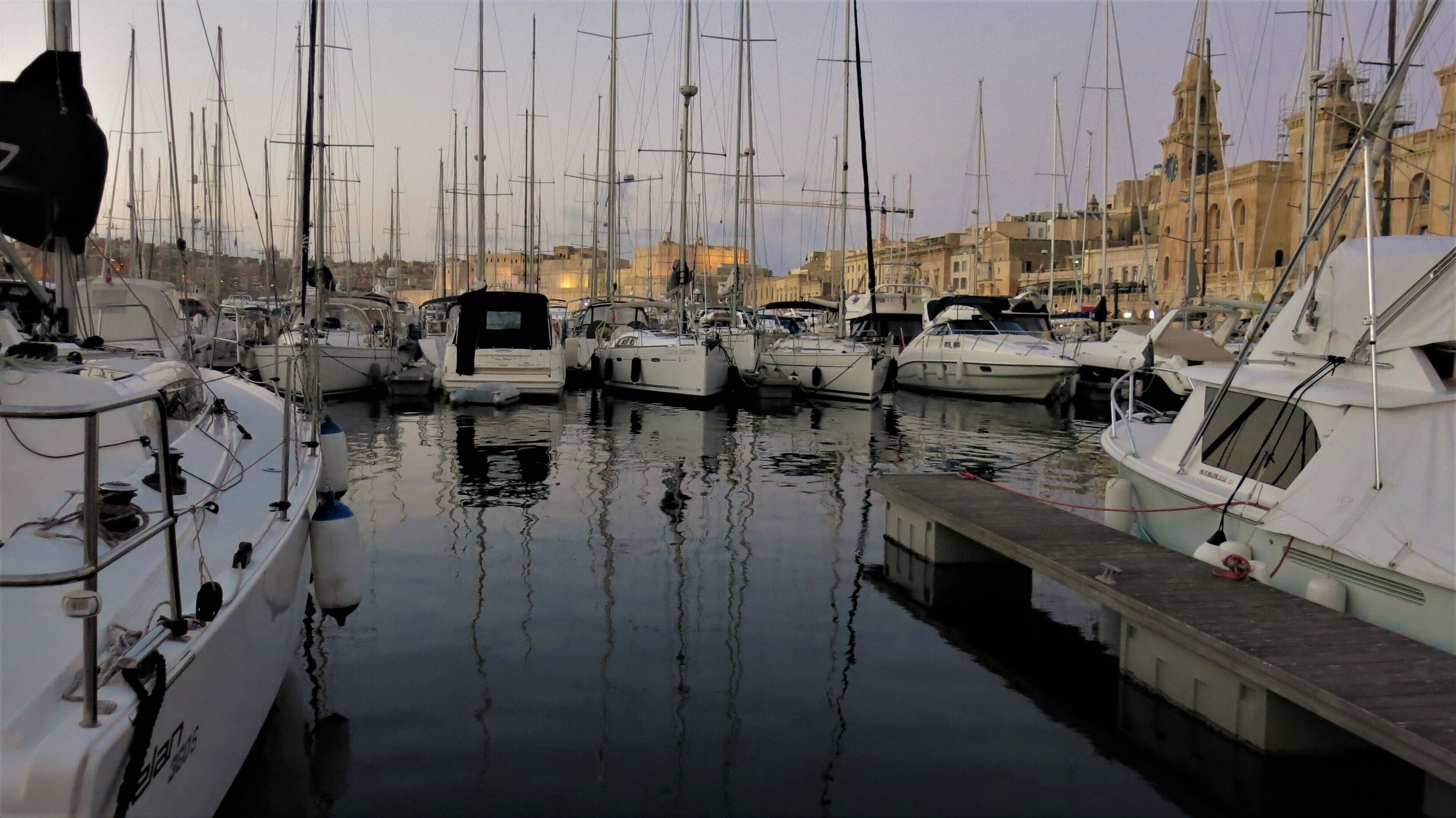A marina with multiple boats docked, a bridge, and a building with a clock tower in the background.