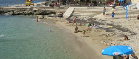 Una playa con agua cristalina, sombrillas y gente.