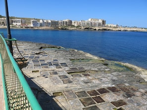 Stroll along the seafront promenade, bordered by a green railing, with the ocean stretching out before you.