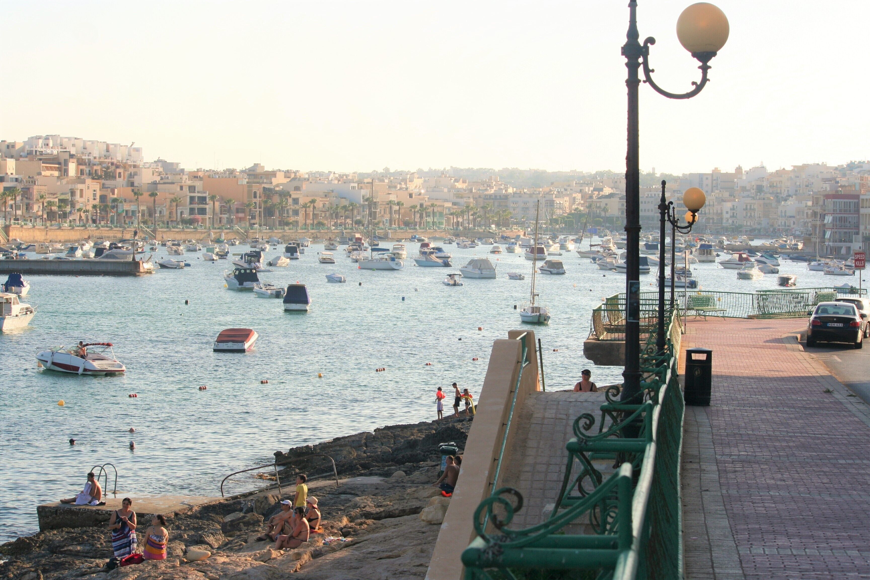 A harbor with boats, a stone wall, and a paved walkway.