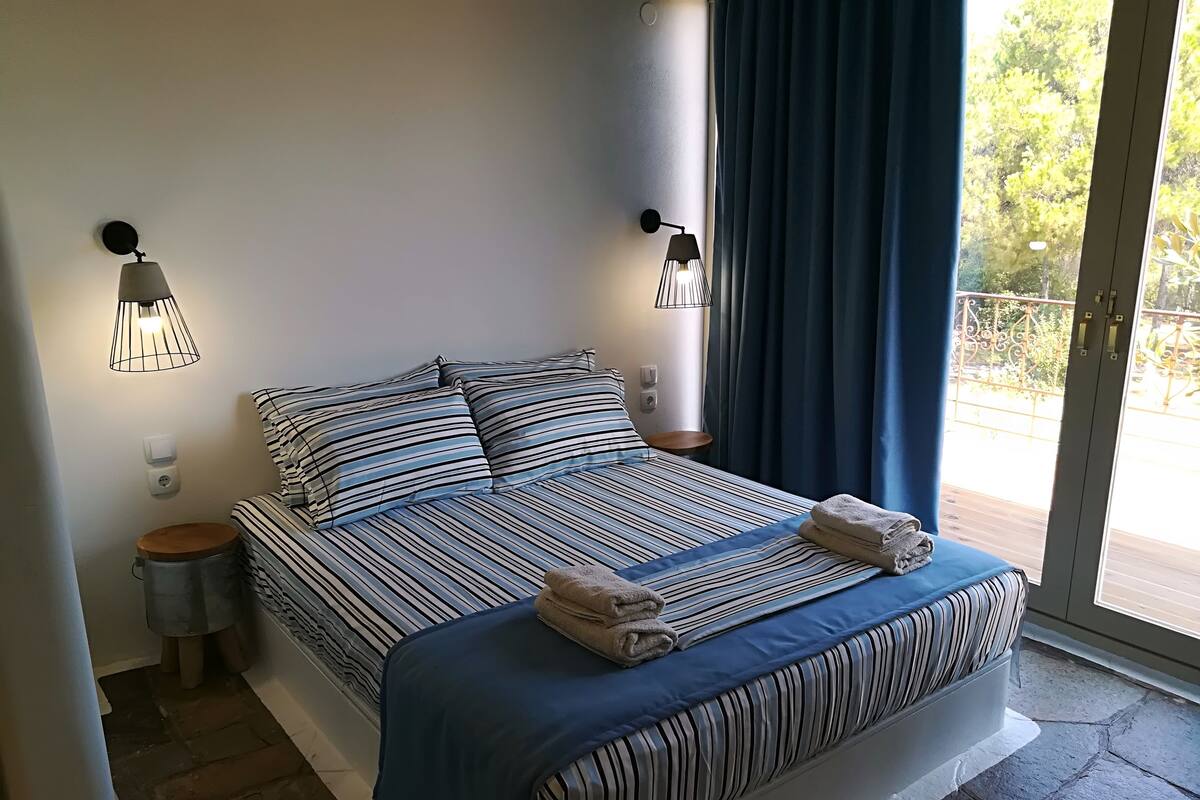 A bed with striped bedding, two bedside lamps, a nightstand, and a view of the outdoors through a glass door.