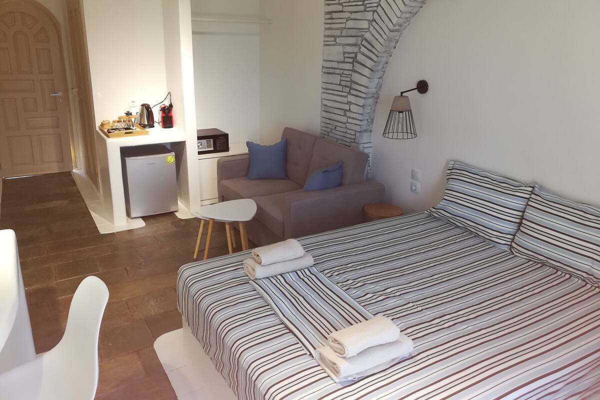 A hotel room with a bed, a sofa, a small table, a desk with a microwave, and a kitchenette.
