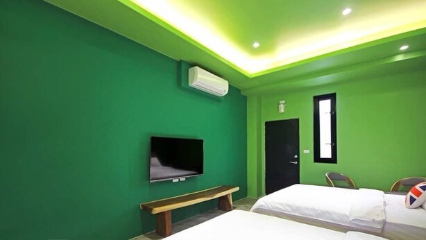 Ein Zimmer mit grünen Wänden, einem flachbildfernseher an der Wand, einer Bank, einem Bett mit weißer Bettwäsche und einer Tür mit Fenster.