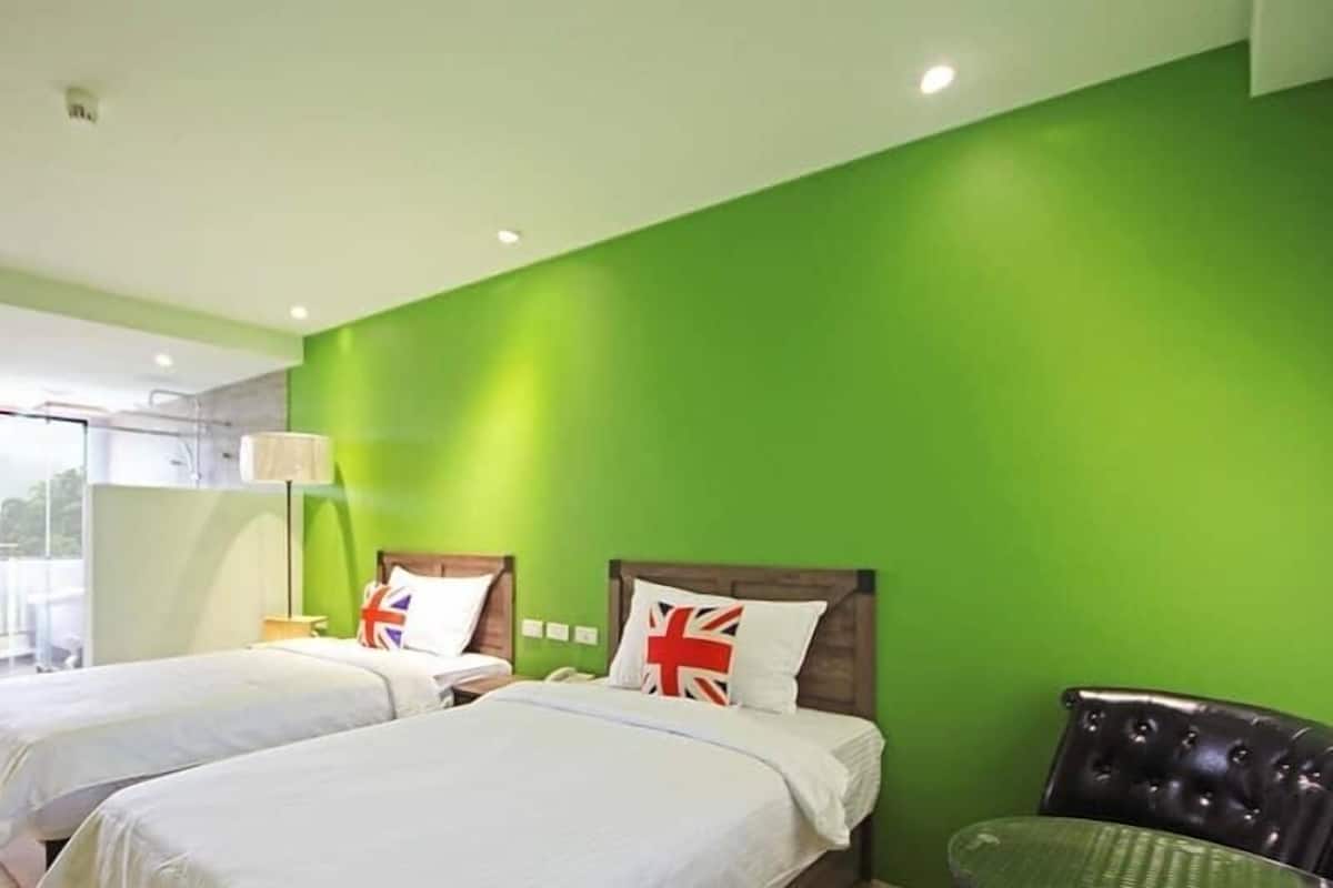 A hotel room with two beds, a green wall, and a balcony with a view.
