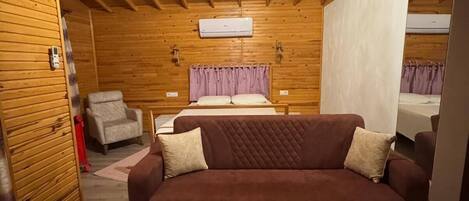 A cozy room with a brown sofa, a patterned rug, wooden walls, a ceiling fan, and a bed with a purple headboard.