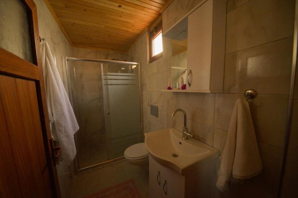 A bathroom with a shower, toilet, sink, and wooden ceiling.