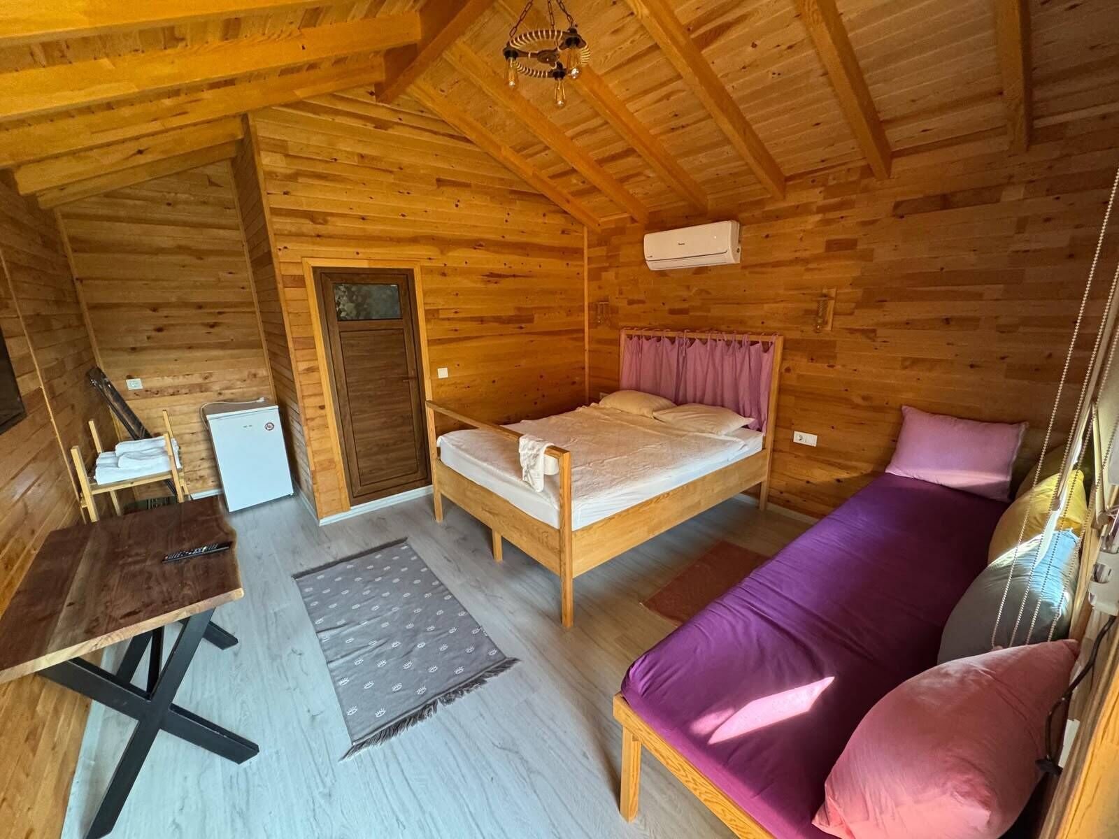 A wooden cabin interior with a bed, a sofa, a table, and a small desk.
