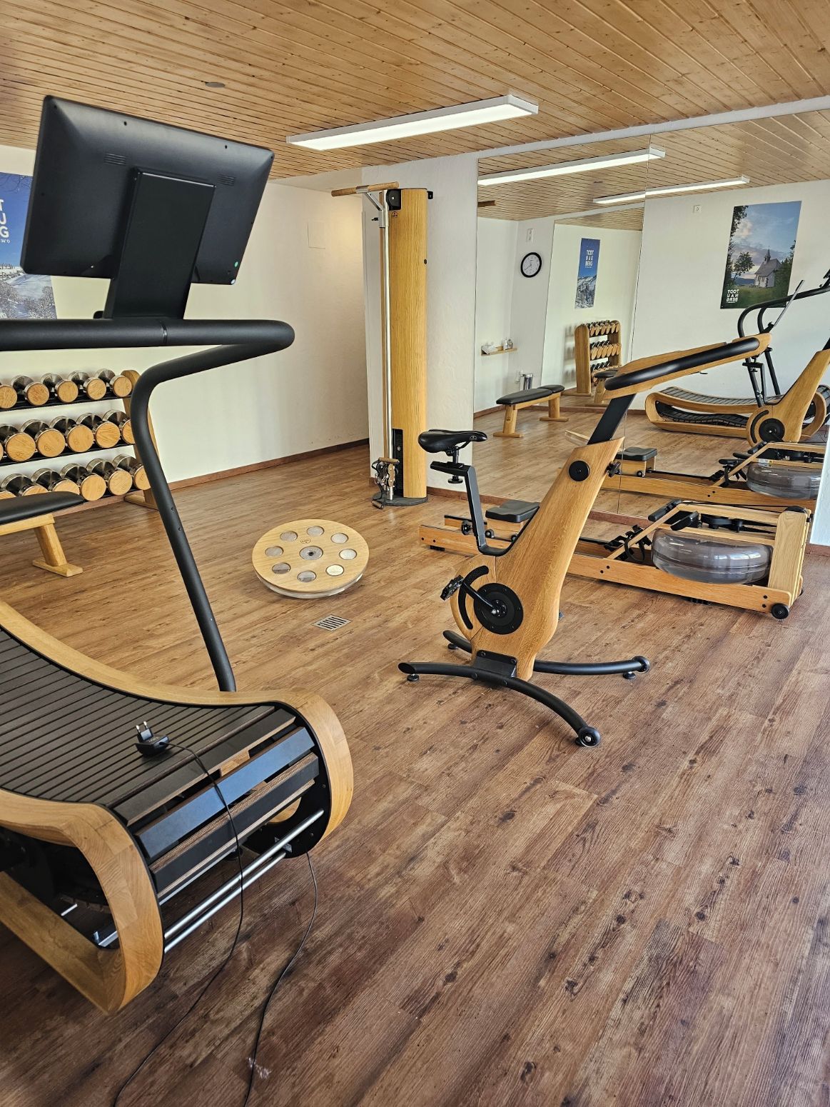 Un gimnasio con equipamiento de ejercicio, suelo de madera y un muro con espejos.