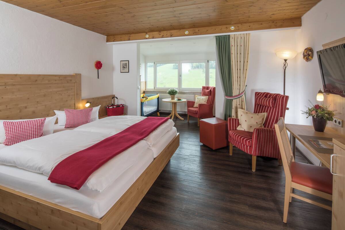 Une chambre d’hôtel avec un lit en bois, une petite table avec une plante, une chaise et un bureau avec une lampe.