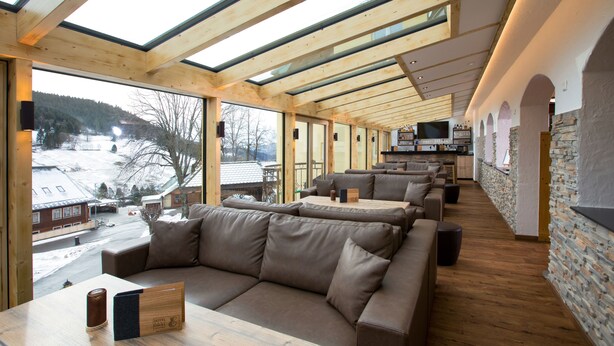 Un interior moderno con techo de madera, ventanas amplias, un sofá y una pared de piedra.