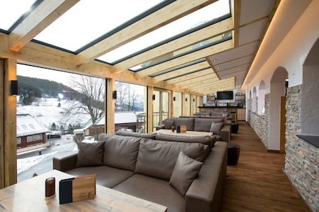 A modern interior with a wooden ceiling, large windows, a sofa, and a stone wall.